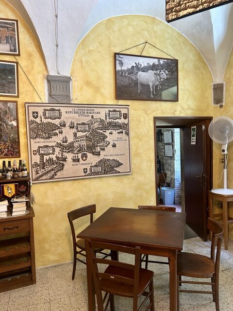 Tavolo in legno nella sala interna dell'enoteca, tra stampe d'epoca